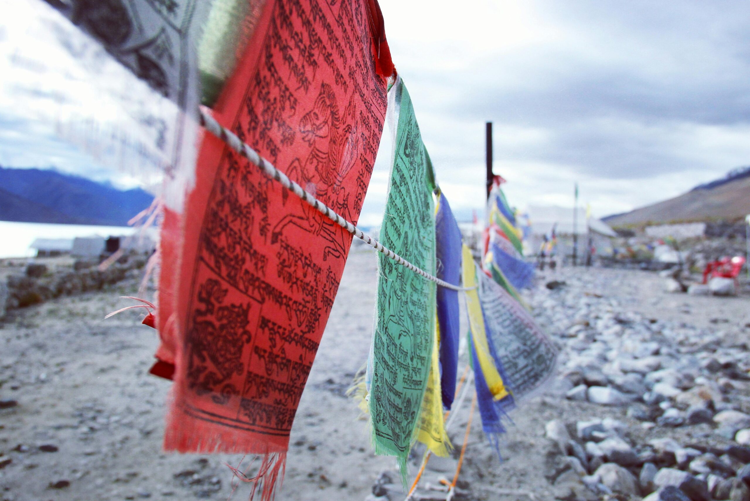 Vibrant Tibetan prayer flags fluttering over a rocky Ladakh landscape in summer.
